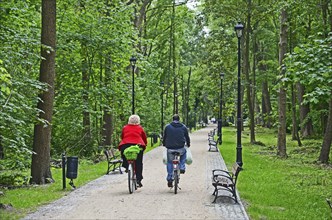 Two cyclists on a narrow road with benches through a forest in Swinoujscie, Swinemünde, West