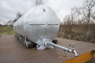 Silver Metal water tank with water pump in front on a trailer outdoors next to an agricultural