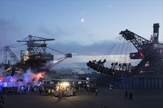 Evening atmosphere with festival visitors and beer stand between excavators at the Melt Festival in