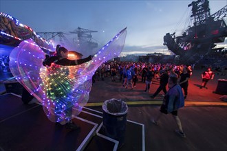 Festival visitor with a bright dress between excavators in the evening at the Melt Festival in