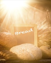 Bread and wheat on the wooden table in autumn field. Blackboard with copyspace