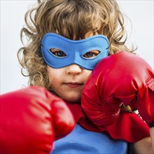 Superhero kid wearing boxing gloves against blue sky background. Girl power and feminism concept