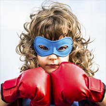 Superhero kid wearing boxing gloves against blue sky background. Girl power and feminism concept