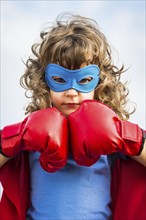 Superhero kid wearing boxing gloves against blue sky background. Girl power and feminism concept