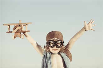 Happy kid playing with toy airplane against blue summer sky background