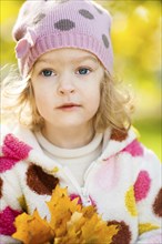 Beautiful child with yellow maple leaves in autumn park