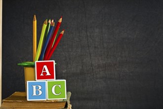 ABC and multicolored pencil on old textbook against blackboard in class. School concept