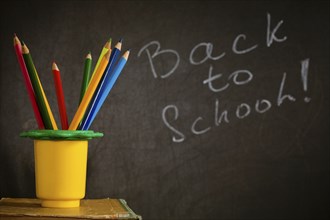 Coloured pencil in holder against blackboard with text