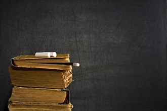 Chalk and pencil on old textbook against blackboard in class. School concept