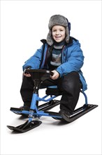 Little smiling child boy sitting on snow scooter or snowmobile toy white isolated