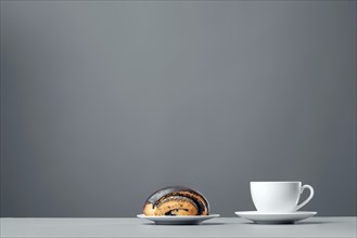 White mug and a chocolate muffin with poppy seeds on a gray background