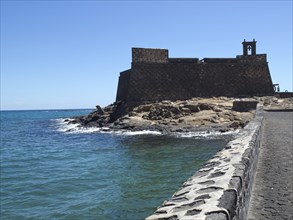 Historic castle with stone walls on the coast, in the background the blue sea and sky, arrecife,