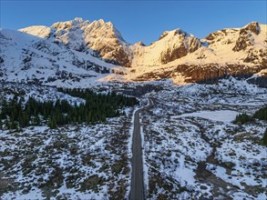 Aerial view of road in front of steep mountains, winter, sunrise, Flakstadoya, Lofoten, Norway,