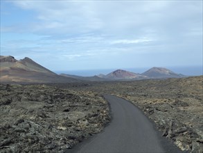 Tarmac road through a lava field in a mountainous landscape under a cloudy sky in Lanzarote,