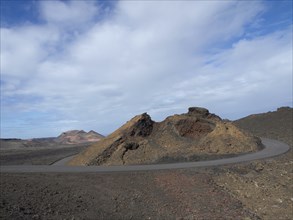 A winding tarmac road through a volcanic hilly landscape under an overcast sky, arrrecife,