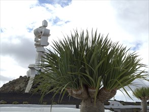 Modern sculpture in a landscape with palm trees under a cloudy sky on Lanzarote, arrecife,