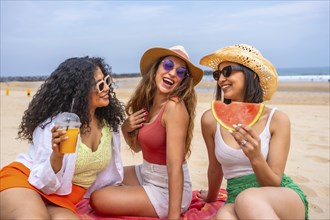 Multiethnic friends enjoying summer on the beach on vacation, outdoors laughing sitting on the sand