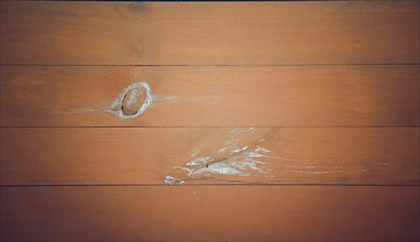 A close-up of orange-brown wooden planks with a noticeable knot and scratches, showcasing a rustic