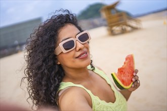 Selfie of Latin woman in summer on the beach on vacation with hat and a watermelon