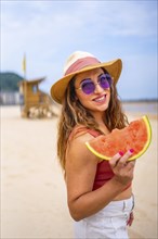 Very cheerful caucasian woman in summer on the beach on vacation with hat and a watermelon