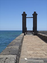 A stone footbridge leads to a Tor tor with a view of the blue sea and sky, arrecife, Lanzarote,