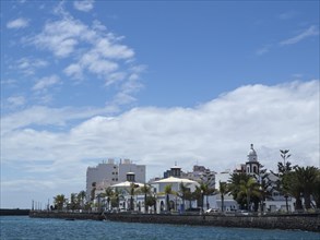 City view with a row of buildings and palm trees along the sea shore under a blue sky, arrecife,