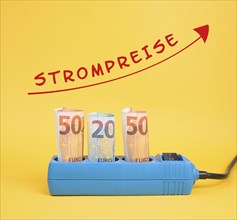 Euro banknotes in a power outlet, increasing prices for electricity is standing in german language