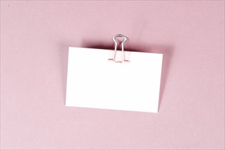 Blank white paper with a paperclip on a pink colored background, copy space for text, reminder or