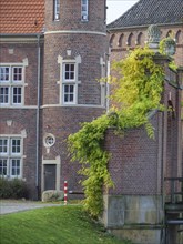 A detail of a historic castle with red brick walls, windows and ivy, embedded in an autumnal