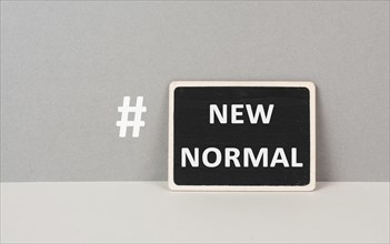 The words new normal with a hashtag are standing on a chalkboard, gray colored background