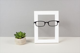 Home interior poster mock up with wooden frame, eyeglasses and cactus in a pot, gray wall