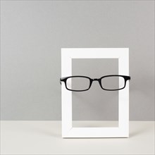 Home interior poster mock up with wooden frame and eyeglasses, gray wall background, copy space for