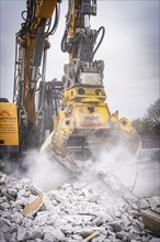 Large yellow excavator with grab crushes concrete rubble and stirs up dust on a construction site,