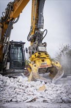 Yellow demolition excavator with grab crushes rubble on a construction site, a large amount of