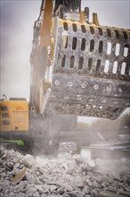 Demolition excavator with a metal grab crushes concrete rubble, raises dust on a construction site,