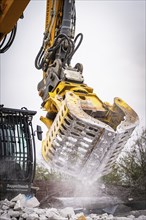 Yellow excavator with a massive metal grab cleans debris on a construction site, water splashes