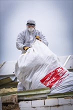 Worker in protective suit and mask handling a large bag of fibre wool on a construction site,