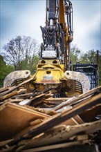 Large demolition machine crushing wood debris in front of a wooded background, demolition site,