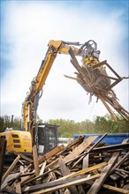 An excavator during demolition work, moving wood and metal under a cloudy sky, demolition site,