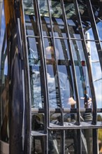 A driver in a construction vehicle, seen through the window with reflections and bars, demolition