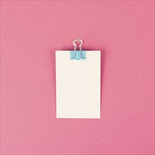 Blank white paper with a paperclip on a pink colored background, copy space for text, reminder or