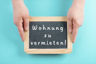 Holding a chalkboard in the hands, apartment for rent is standing in german language on the sign,