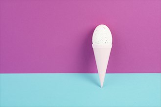 Ice cream cone with an egg, pink and blue background, copy space, easter holiday, summer season,