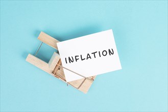 Paper with the word inflation in a mousetrap, high financial burden, increased costs and expenses