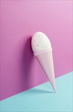 Ice cream cone with an egg, pink and blue background, copy space, easter holiday, summer season,