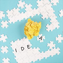 Puzzle on a blue background, yellow crumbled paper, word idea is standing on the jigsaw pieces,