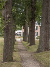 Narrow path lined with trees, leading to a brick building in the background, groenlo, gelderland,