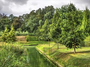 Green parkland with canal, fenced by trees, reflecting water and green meadow, groenlo, gelderland,