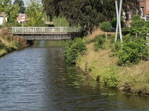 Quiet river course with narrow bridge, surrounded by lush vegetation and trees in an idyllic