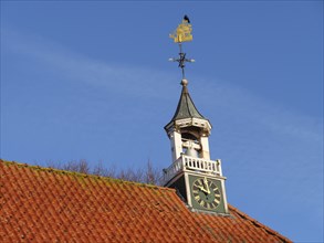 Church tower with clock and golden weather vane under a clear sky, greetsiel, east frisia, germany